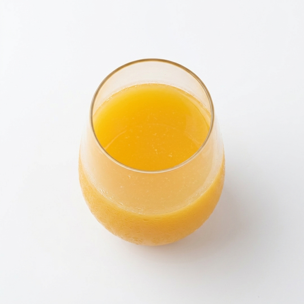 Vaso de cristal moderno lleno de zumo de naranja recién exprimido, de color naranja intenso, sobre fondo blanco puro.