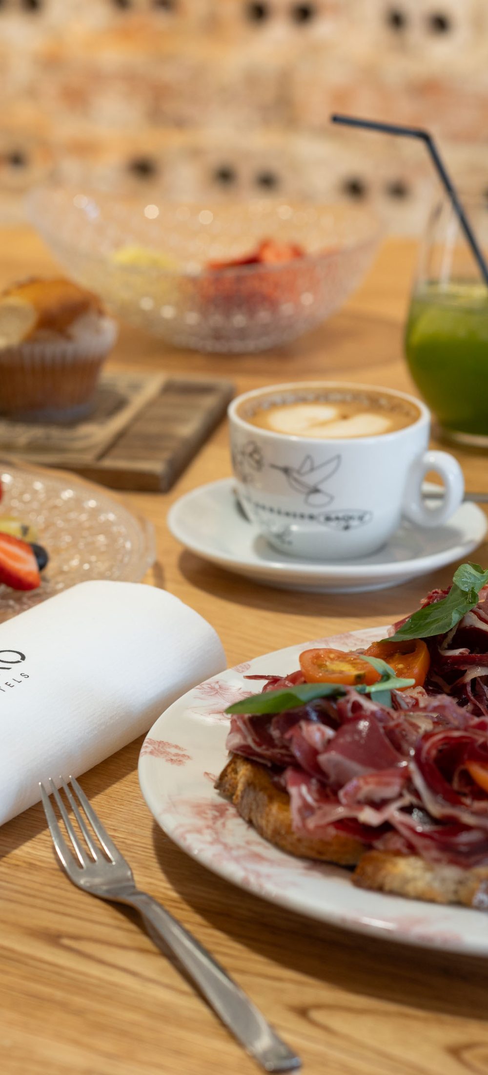Desayuno Tayko Bilbao, mesa con tostada de jamón, ensalada de frutas, croissant, café y zumo verde, con servilleta del hotel
