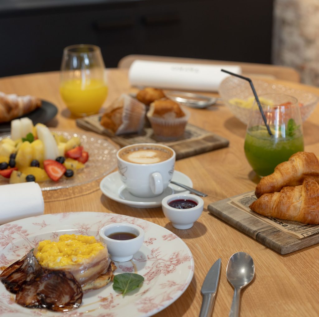 Desayuno en Tayko Bilbao, mesa con zumo de naranja, café con leche, croissant, fruta fresca, huevos revueltos y embutido