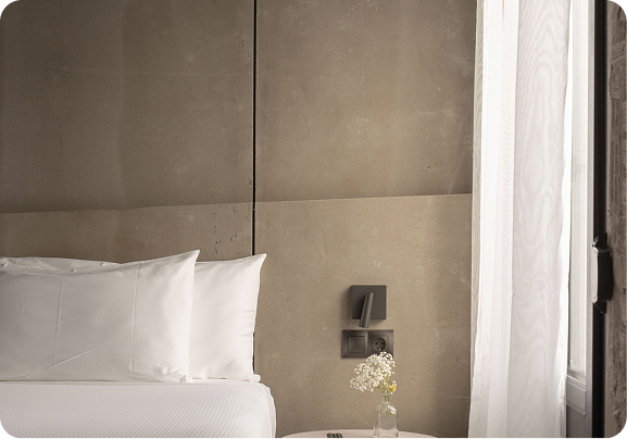 A bed with a stone-panelled headboard, a reading lamp and a vase of flowers by the window at Tayko Bilbao