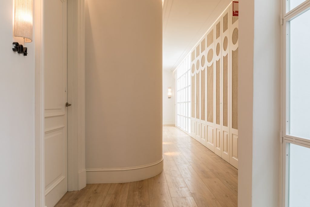 Corridor of the hotel Tayko Sevilla, bright corridor with light wooden floor, white walls and decorative rattan lattice, modern design in a historic building.